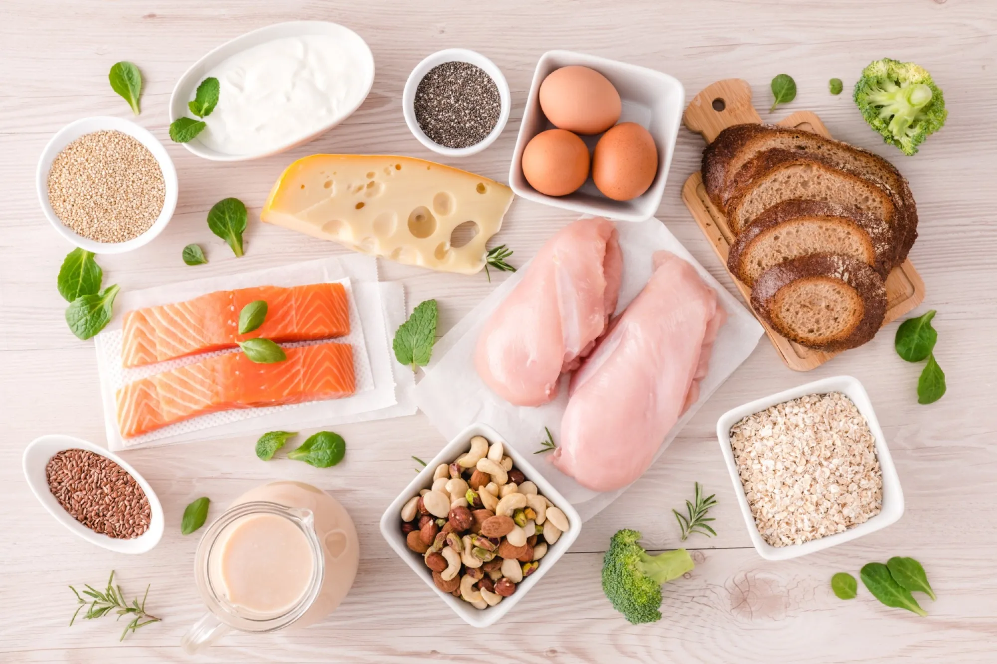 Assortiment d'aliments sains sur une table : saumon, poulet, œufs, pain complet, fromage, graines et fruits secs
