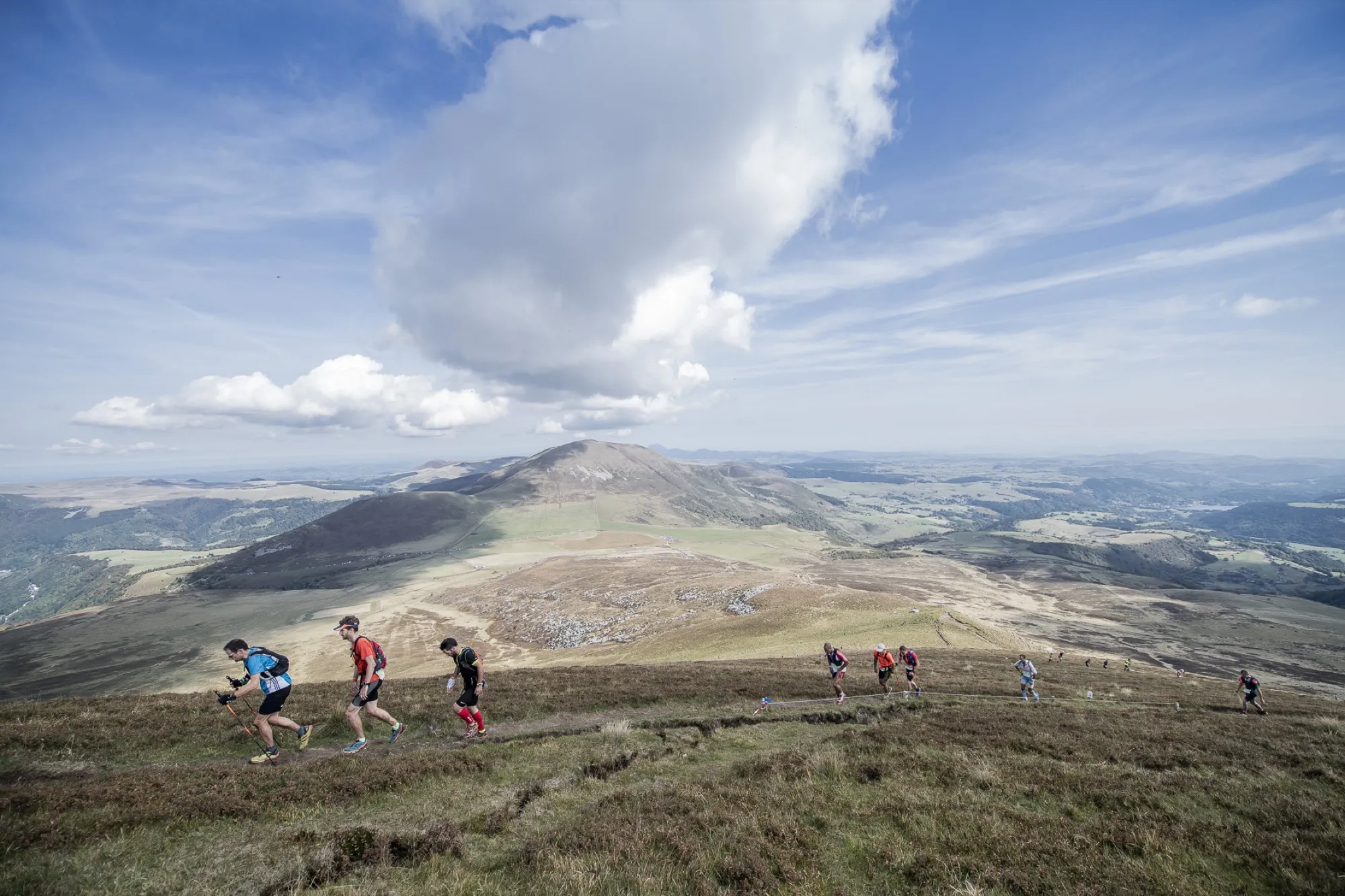 Groupe de traileurs sur un plateau d'altitude du Sancy, montagnes et nuages en arrière-plan