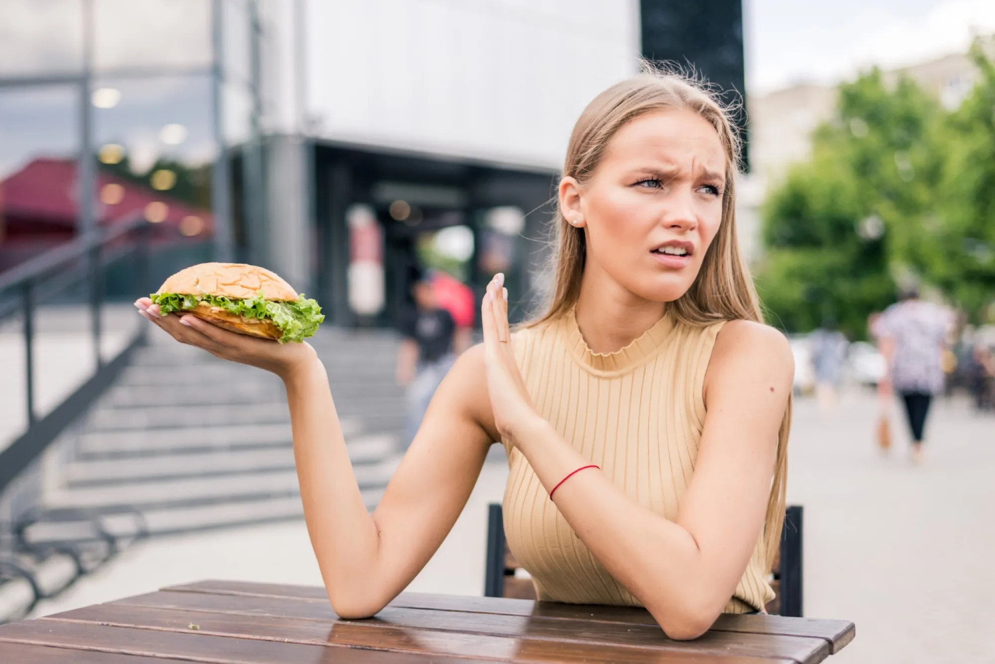 Femme repoussant un hamburger avec une grimace, assise à une terrasse