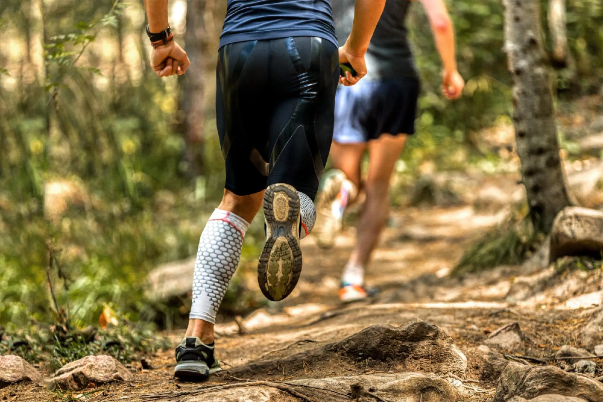Jambes de traileurs en pleine course sur un sentier de forêt