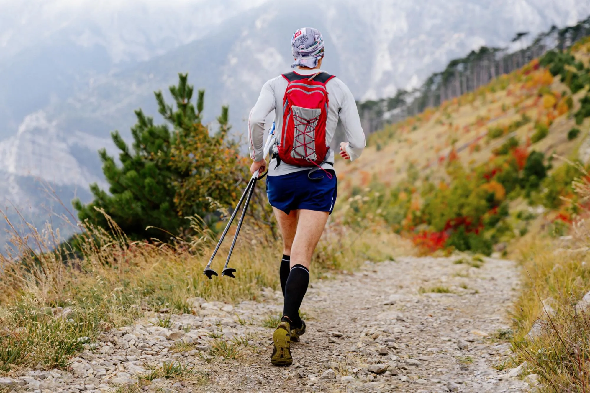 Traileur avec bâtons et sac rouge sur un chemin de montagne