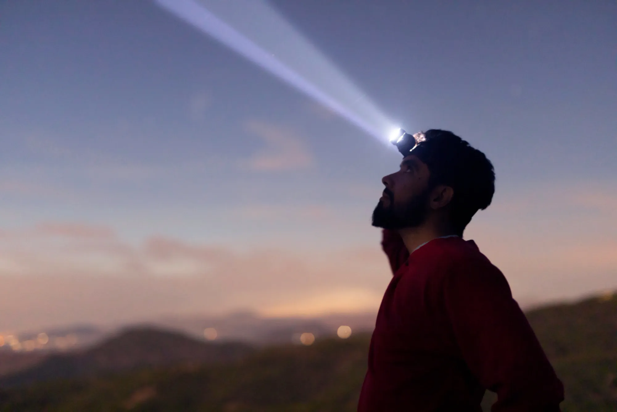 Coureur de nuit, frontale allumée, sur une hauteur au-dessus des lumières de la ville