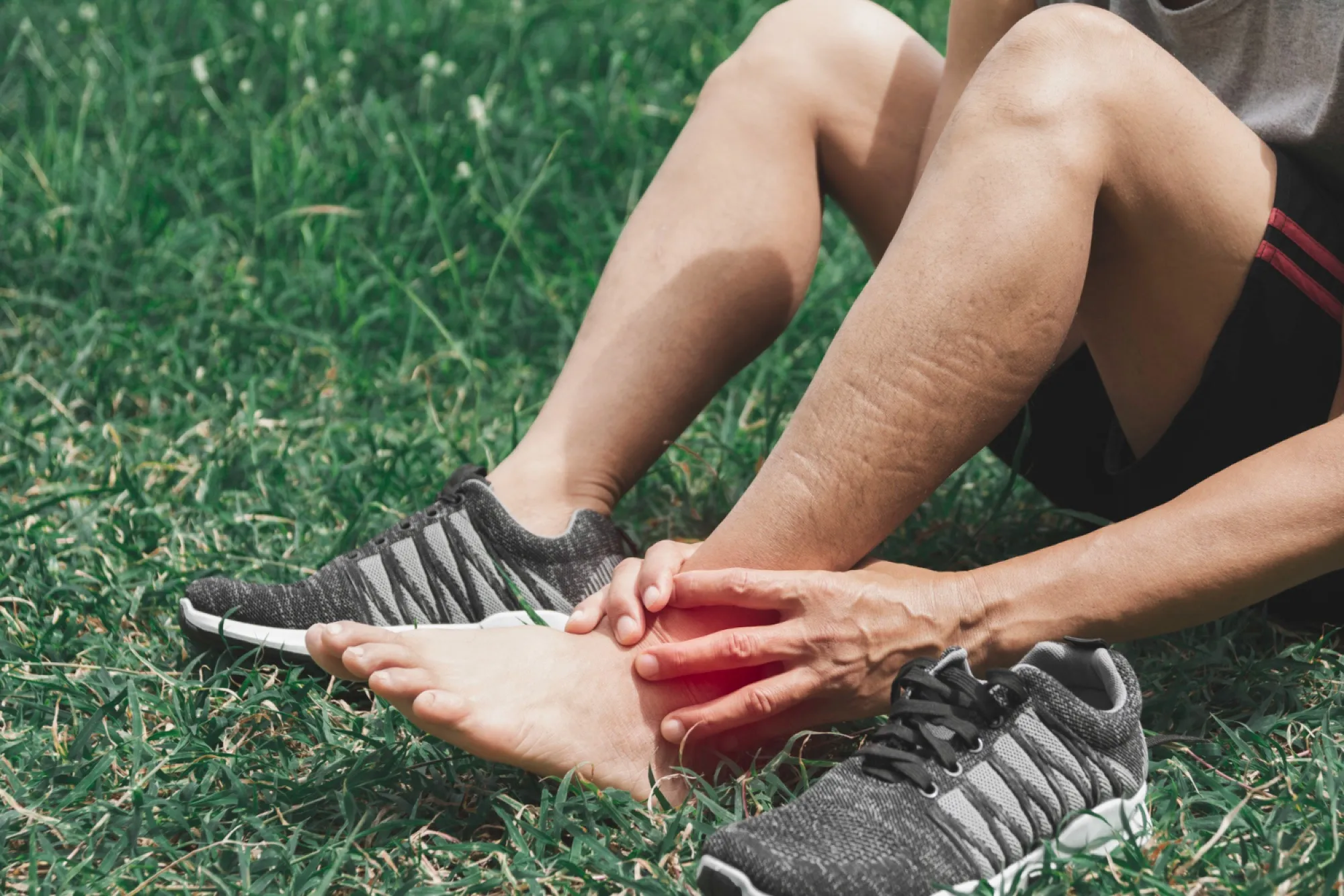 Coureur assis dans l'herbe se tenant la cheville douloureuse